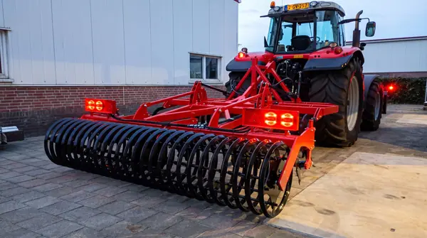 Rode cultivator met kooirol en brandende achterlichten in de schemering