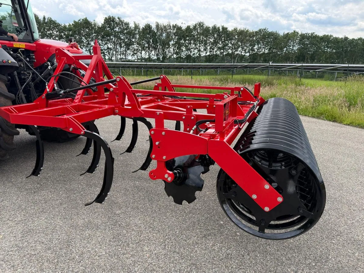 Rode cultivator met zwarte tanden, schijven en kooirol achter een trekker