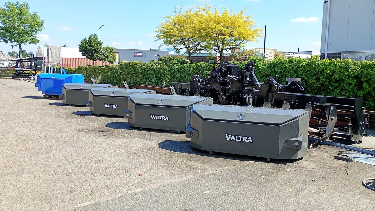 Rij grijze frontgewichten met Valtra-logo en een blauw gewicht